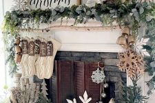 frmhouse Christmas decor with large wooden snowflakes, evergreens, bells, stockings and trees on the mantel