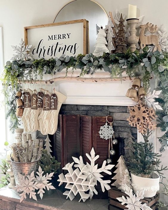 frmhouse Christmas decor with large wooden snowflakes, evergreens, bells, stockings and trees on the mantel