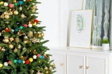 gold ornaments and a colorful pompom garland over the tree is a fun and whimsy idea for Christmas