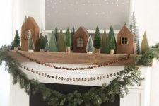 rustic woodland Christmas mantel decor with wooden houses, bottle brush Christmas trees, a nut, berry and evergreen garland on the mantel