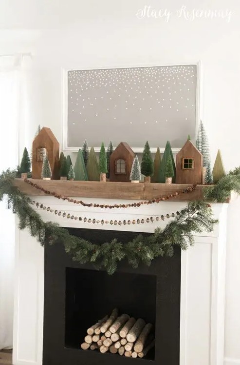rustic woodland Christmas mantel decor with wooden houses, bottle brush Christmas trees, a nut, berry and evergreen garland on the mantel