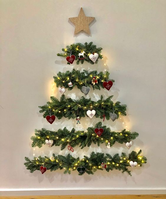 A catchy wall mounted Christmas tree of evergreens, lights, ornaments and a star topper is amazing