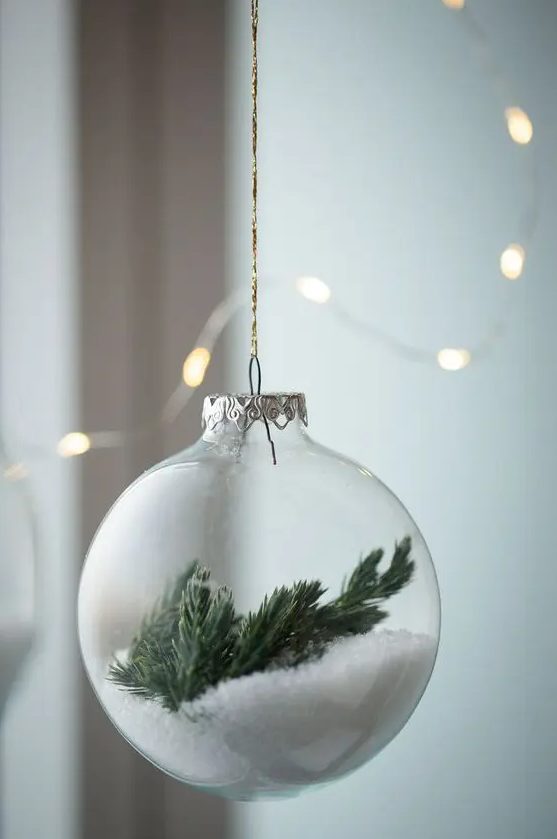A clear glass Christmas ornament with faux snow and evergreens is a dreamy winter inspired decor idea