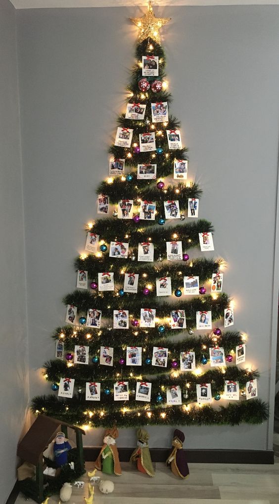 A lovely wall mounted Christmas tree of green tinsel, lights, colorful ornaments and photos plus a star topper