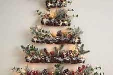 a lovely woodland wall-mounted Christmas tree of branches, evergreens, berries, snowy pinecones and lights