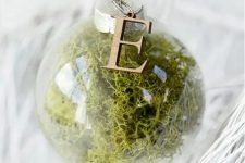 a moss-filled clear glass Christmas ornament with a wooden monogram on top is a cool woodland decoration for your tree