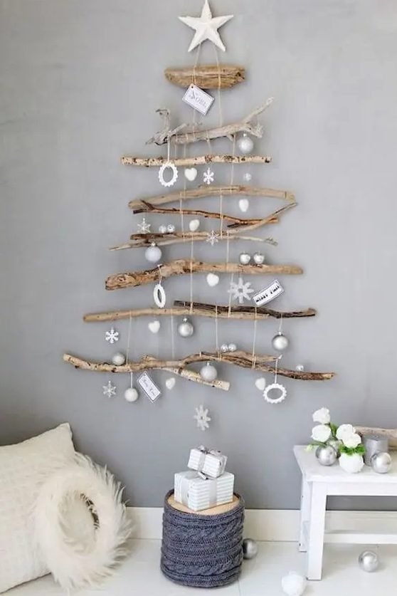 A natural wall mounted Christmas tree of various branches and with white and silver ornaments hanging down