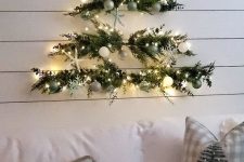 a pretty wall-mounted Christmas tree of greenery, white, green and silver ornaments and lights is fresh and cool