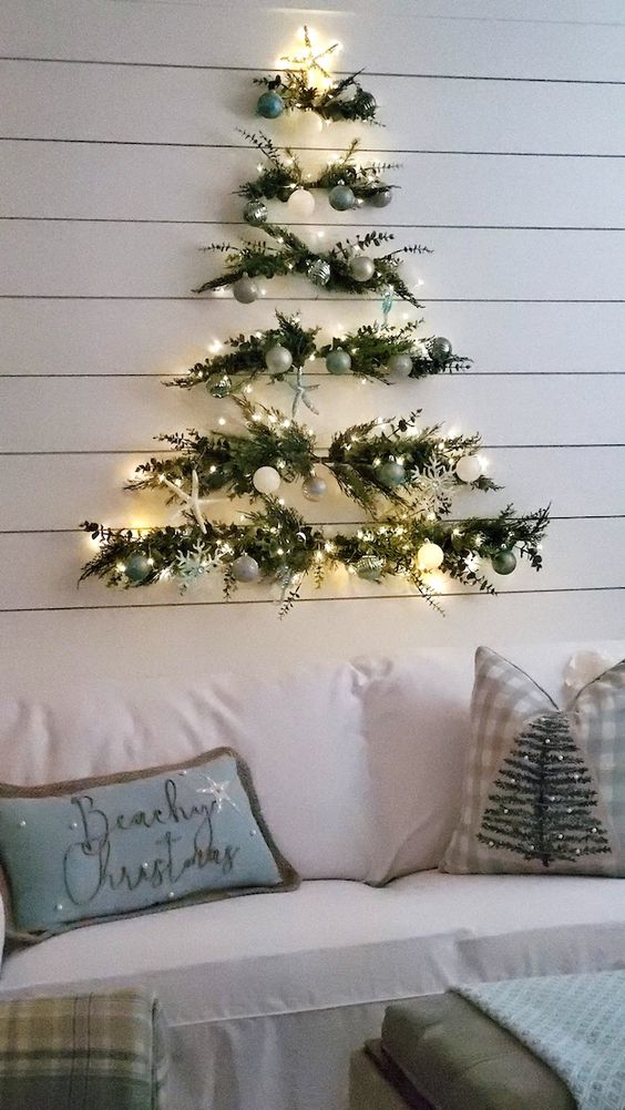 A pretty wall mounted Christmas tree of greenery, white, green and silver ornaments and lights is fresh and cool