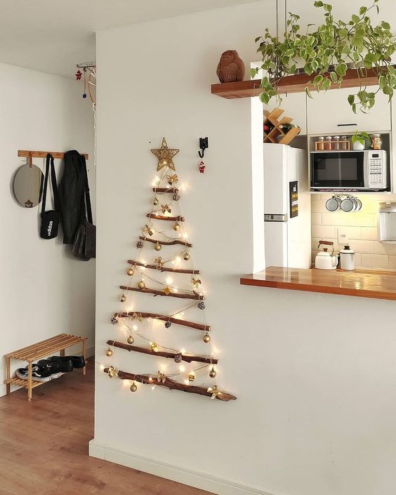 A small and pretty wall mounted Christmas tree of branches, lights and small ornaments plus a star topper