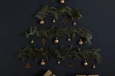 a stylish wall-mounted Christmas tree on a black wall of evergreens, lights and brass ornaments