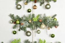 a wall Christmas tree of evergreens, berries and muted green ornaments is a chic and catchy decoration