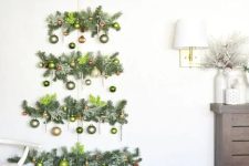 a wall-mounted Christmas tree of evergreens, gold and green ornaments and a snowflake topper is cool