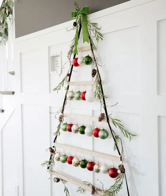 A wall mounted Christmas tree of ledges, rope and colorful ornaments with greenery is lovely