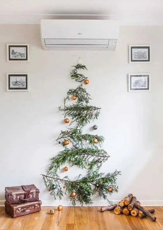 A wall mounted pine branch Christmas tree with gold and grey ornaments is a bold and catchy idea