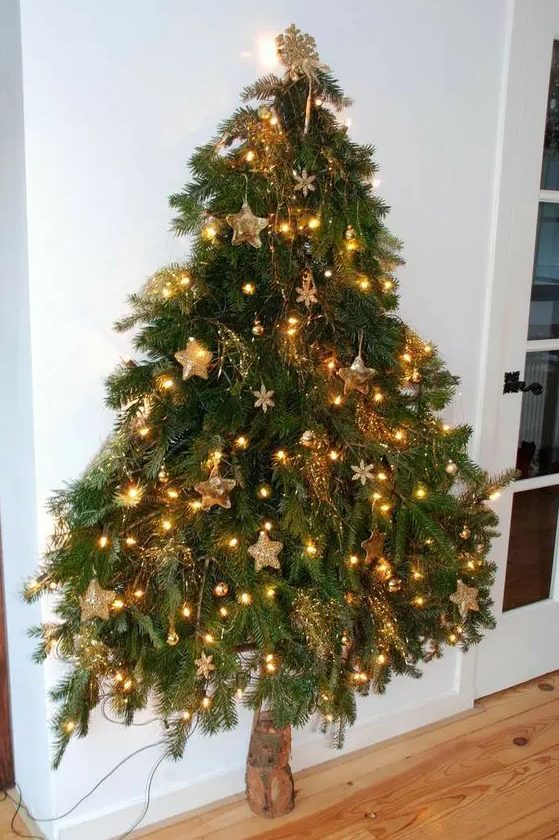 A wall moutned Christmas tree reminding of a real one, with lights, gold ornaments and snowflakes