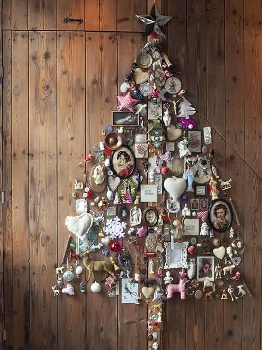 A whimsical wall mounted Christmas tree of figurines, frames, photos and various vintage stuff for a shabby chic space
