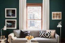 a catchy small living room with dark green walls, a grey sofa with printed pillows, a printed rug, an oval table and some artwork