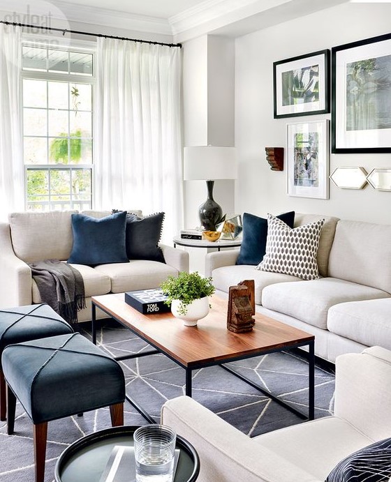 a lively living room with white furniture, navy stools, a wooden table, a printed rug, printed pillows and airy curtains