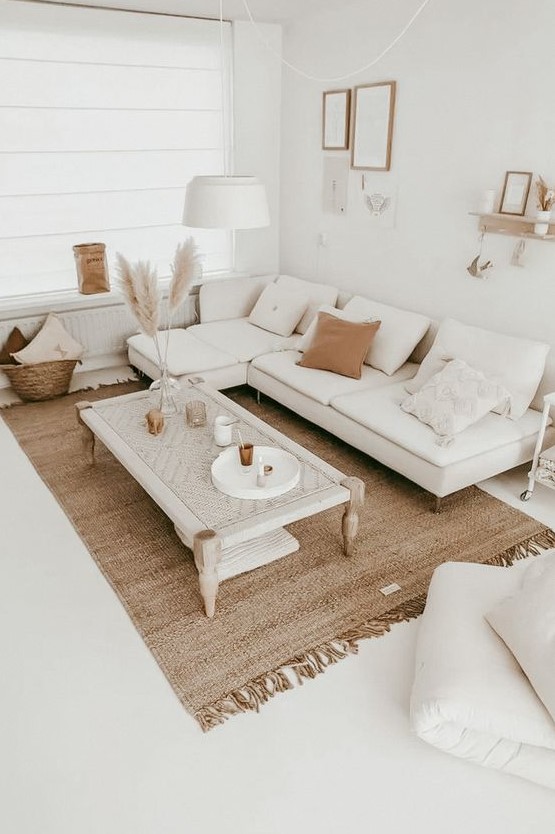 a neutral boho living room with a white sectional, a woven table, a jute rug, pampas grass, a gallery wall and lots of pillows