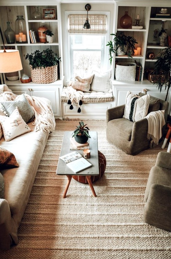 a neutral boho living room with lots of texture, potted greenery, a sofa, chairs and a window seat plus a leather ottoman