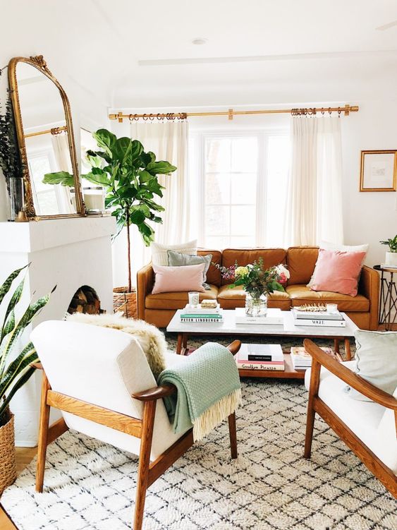 a neutral living room with a fireplace, an orange leather sofa, a coffee table, neutral chairs, a printed rug and potted plants