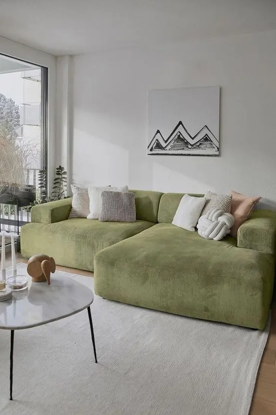 a neutral living room with a low green sofa and neutral pillows, a coffee table with some decor, a neutral rug and a fun artwork