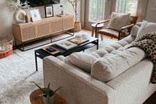 a neutral modern living room with a cane TV unit, a neutral sofa, a leather chair, a black coffee table and some plants