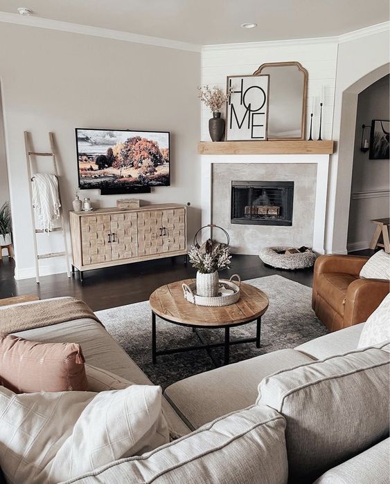 a neutral small living room with a grey sectional, a pretty credenza, a fireplace, a leather chair, a coffee table and some decor