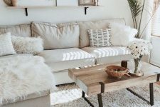 a neutral small living room with a sectional sofa, a wooden table, lots of fur pillows and a gallery wall on a shelf