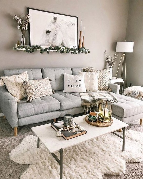 a pretty boho living room with a grey sofa, a white table, layered rugs, neutral tables, some candles and an artwork