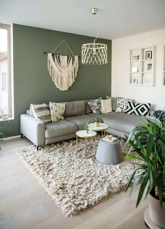 a pretty living room with a green accent wall, a grey sectional, some boho decor and printed pillows, a fluffy rug and coffee tables