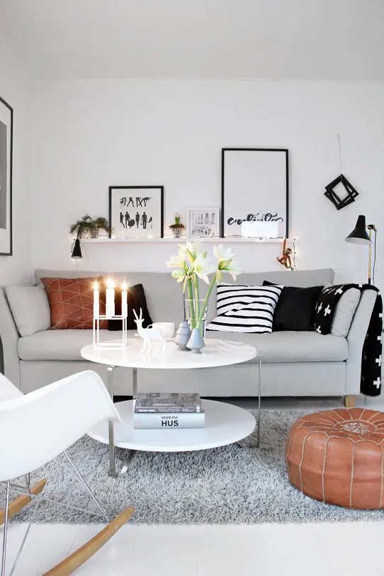 a small Scandinavian living room done in neutrals, with touches of black, printed pillows and string lights and lamps