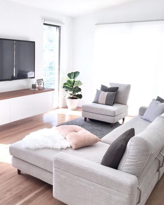 a small Scandinavian living room with a floating TV unit, a TV, a grey sofa, a chair and some pillows is welcoming