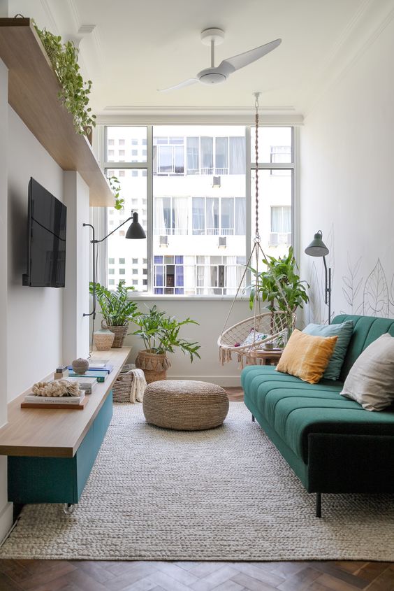 a small and bright living room with an open shelf, a green TV unit, a green sofa, some potted plants, a chair and lamps