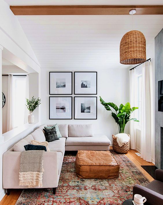 a small and chic living room with a blush sectional, a gallery wall, a printed rug, a leather pouf and a woven pendant lamp