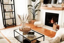 a small and inviting living room with a fireplace, a neutral sectional, a shelving unit, a coffee table, potted plants and pillows