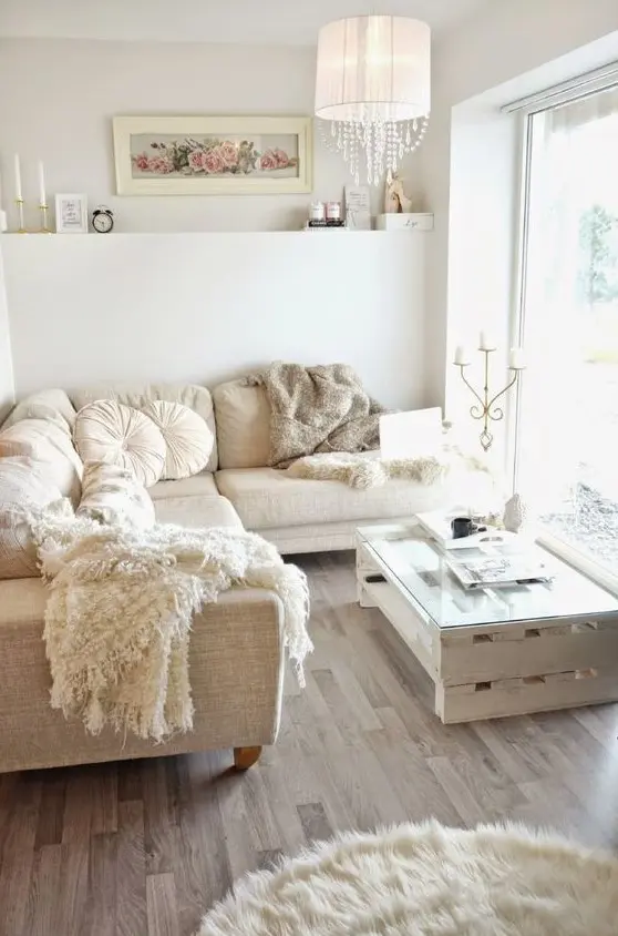 a small and neutral glam living room with a sectional sofa, a pallet table, a fur rug, a lamp with crystals