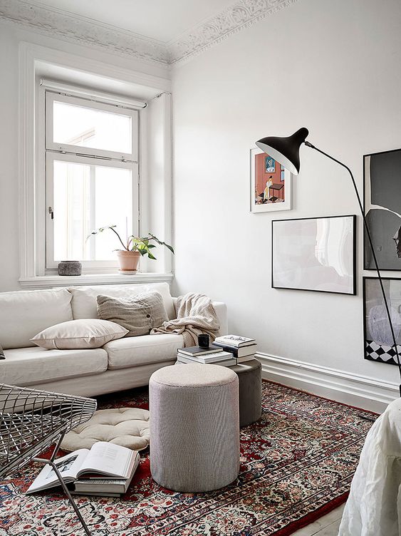 a small and welcoming living room with a neutral sofa, a couple of poufs, a chair, a gallery wall and a printed rug