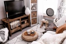 a small boho living room in neutrals, with a white sofa, woven items, a wooden TV unit, stars and a sunburst mirror on the wall