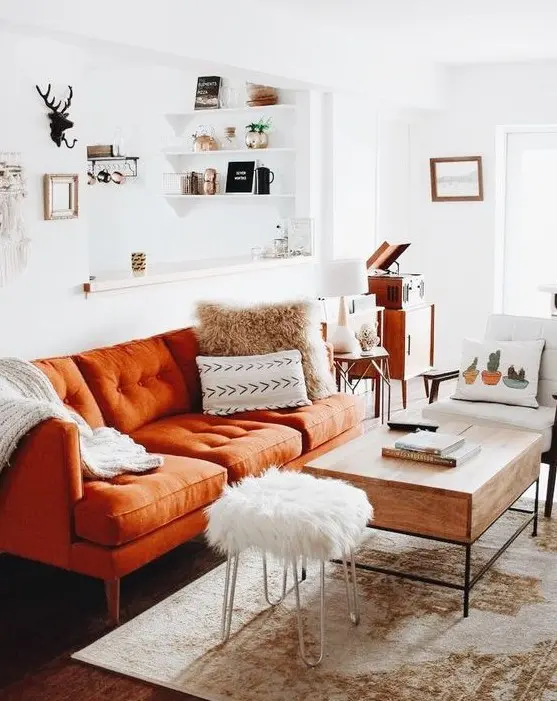 A small boho living room with a rust colored sofa, printed pillows, a wooden table, mid century modern furniture and a boho rug