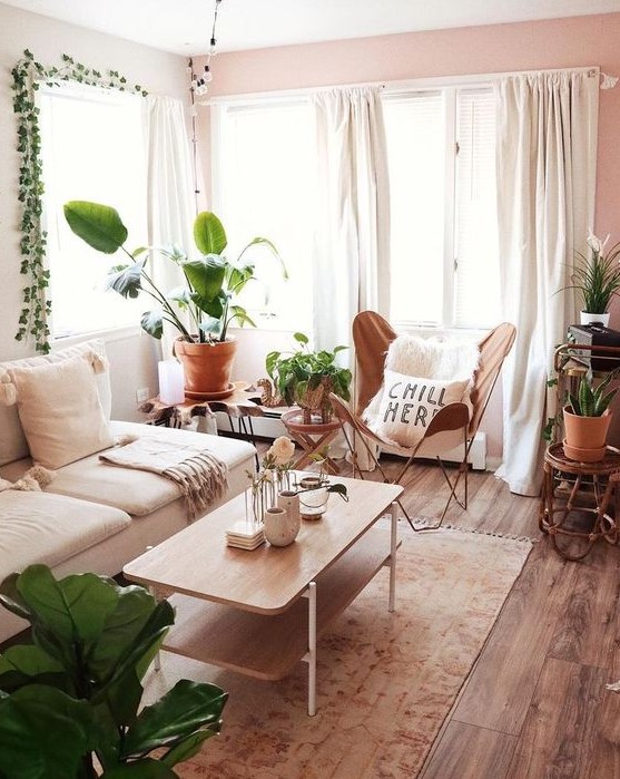 a small boho living room with a white sofa, a leather butterfly chair, a wooden table and lots of plants on stands