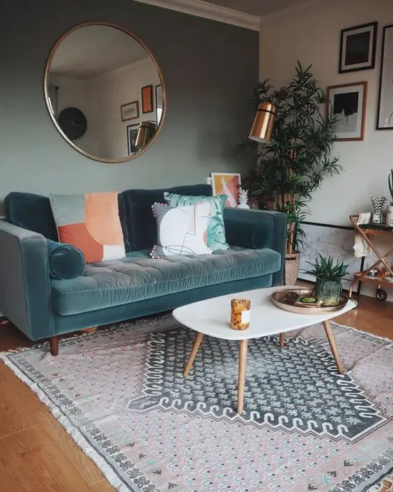 a small living room with a green accent wall, a blue sofa with printed pillows, a printed rug, a coffee table, a bar cart and greenery