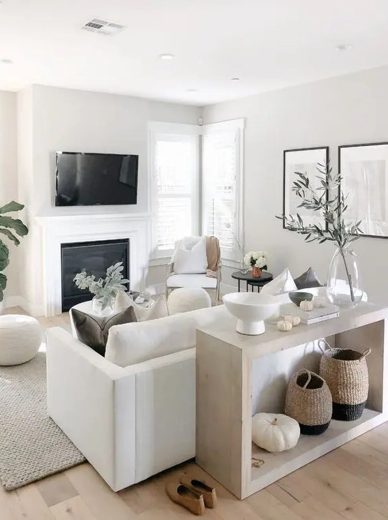 A small neutral living space with a white sofa and chairs, a built in fireplace, a console and some accessories and greenery to refresh the space