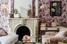 a sophisticated living room with pink floral wallpaper, a creamy sofa, a pink floral chair, a coffee table, a fireplace and a chandelier