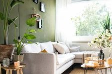 a stylish living room with an olive green accent wall, a neutral sofa, some coffee tables, a gallery wall and some plants