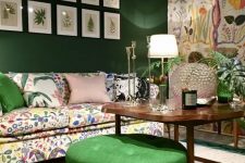 a whimsical living room with an emerald accent wall and a floral one, a crazy floral sofa and a rug, a gallery wall and a green pouf