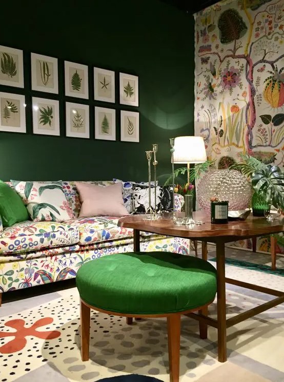 a whimsical living room with an emerald accent wall and a floral one, a crazy floral sofa and a rug, a gallery wall and a green pouf