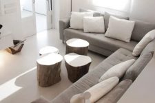 an airy neutral living room in contemporary style with a grey sectional, white pillows, tree stumps, a paper pendant lamp and lots of natural light