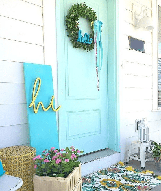 a bright spring porch with a floral mat, potted blooms, a greenery wreath, a modern colorful sign